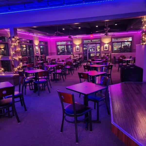 Interior of Shades Bar & Grill with tables and chairs illuminated by purple and blue neon lights.