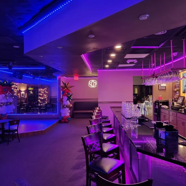 Shades Bar & Grill interior with a long bar, stools, and dining area, illuminated by purple and blue lights.