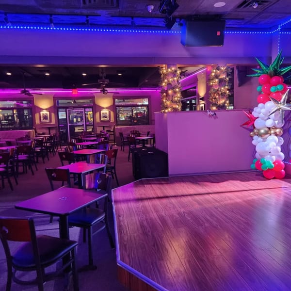 Shades Bar & Grill's interior, featuring a stage, tables, chairs, and festive purple and blue lighting.