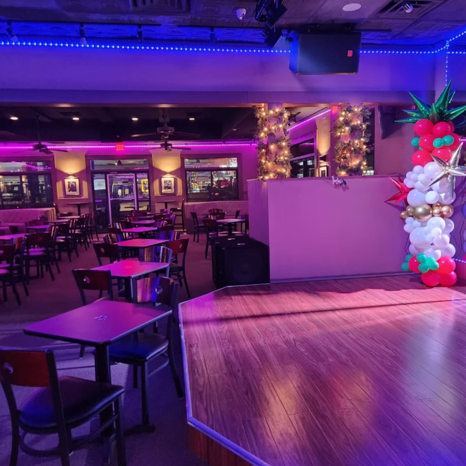 Shades Bar & Grill's interior, featuring a stage, tables, chairs, and festive purple and blue lighting.