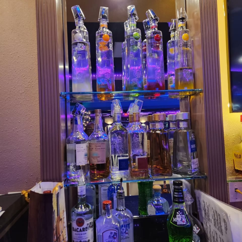 A bar shelf at Shades Bar & Grill displaying various liquor bottles, illuminated by purple and blue lights.